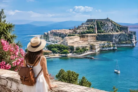 Vrouw met strohoed en rugzak kijkt uit over oude vesting en blauwe zee van Corfu