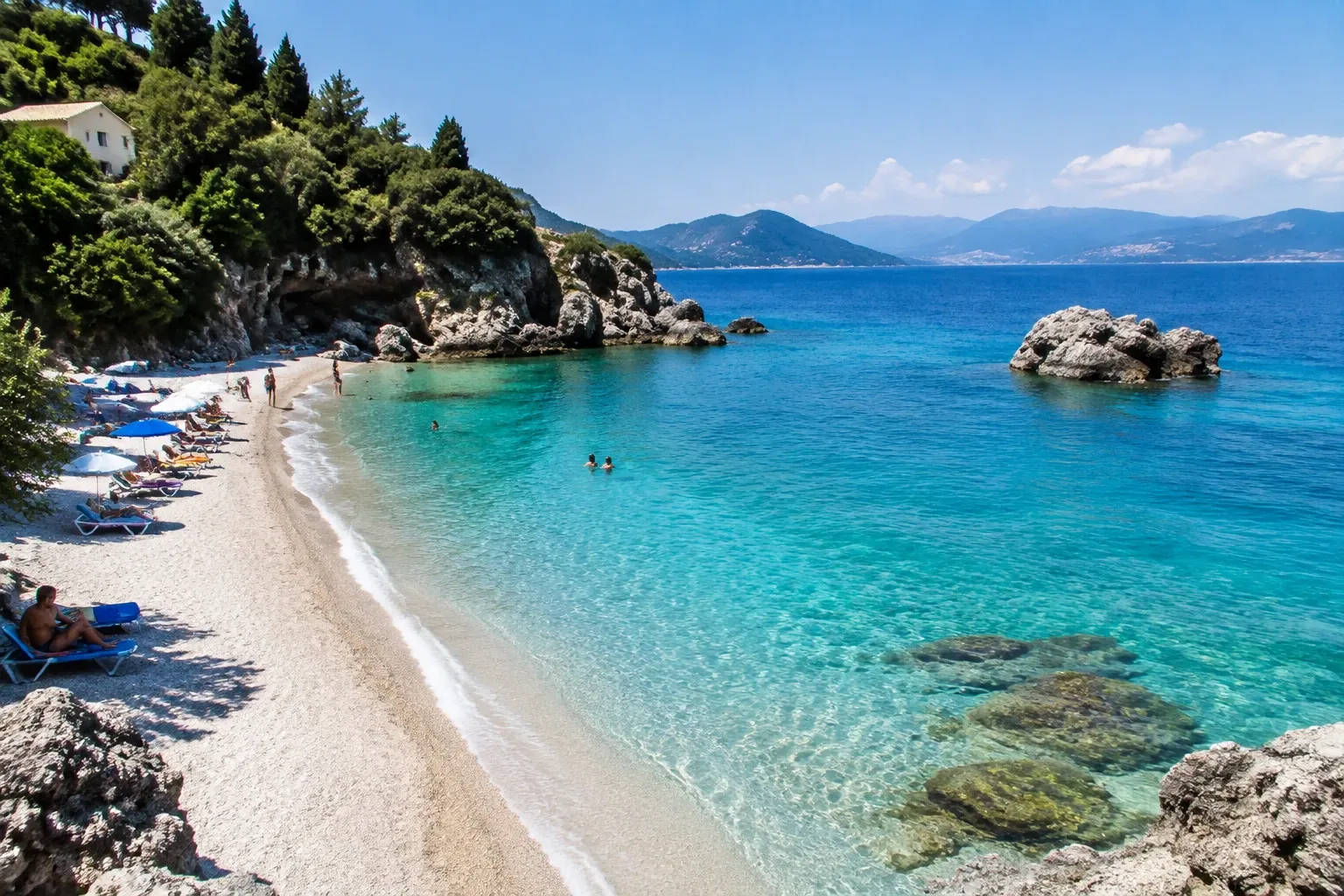 Turquoise water en kiezelstrand met ligstoelen, zwemmers en rotsige kustlijn in Corfu