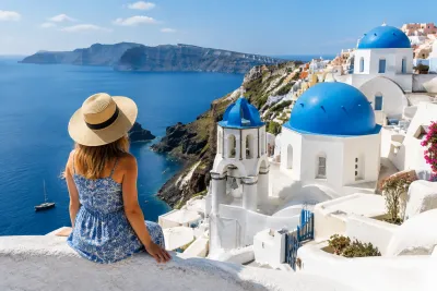 Vrouw met strohoed kijkt over witgekalkt Santorini-dorp met blauwe koepelkerken