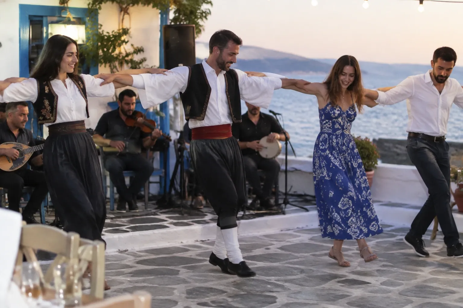 Mensen hand in hand dansen sirtaki op terras bij zee met muzikanten achter hen